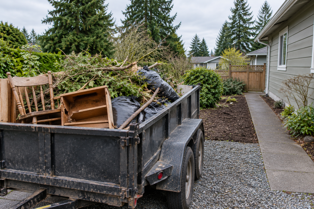 Utility trailer loaded with brush, yard waste and old furniture for property cleanup and junk removal.